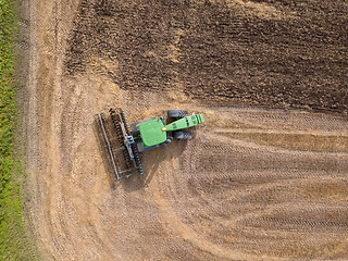 Image showing Top view of green tractor plowing the ground after harvesting on the field in the autumn time. Top view.