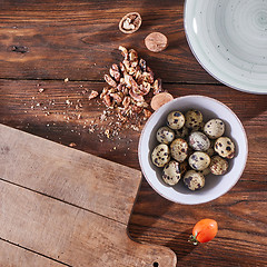 Image showing A bowl with quail eggs, pieces of walnut and a wooden board on the kitchen table with copy space. Ingredients for Healthy Salad. Flat lay