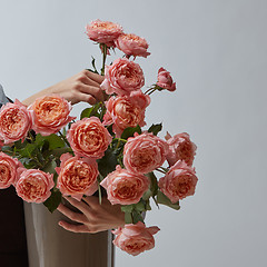 Image showing A big bright bouquet of pink roses in a vase is held by women\'s hands on a gray background with a copy space. Card