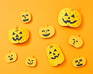 Image showing Pattern of a variety of handcraft paper pumpkins with faces on an orange background with space for text. Layout to Halloween. Flat lay