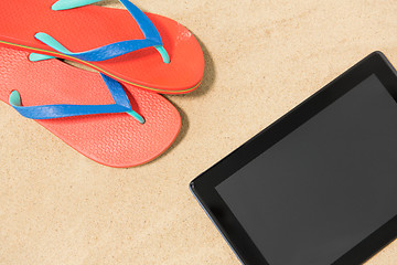 Image showing tablet computer and flip flops on beach sand