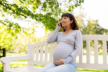 Image showing pregnant asian woman calling on smartphone at park