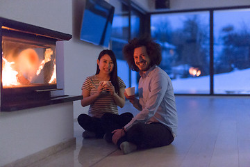 Image showing happy multiethnic couple sitting in front of fireplace