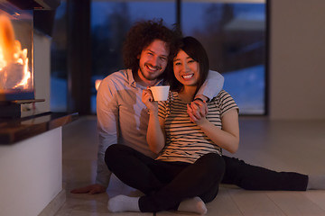 Image showing happy multiethnic couple sitting in front of fireplace