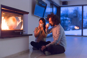 Image showing happy multiethnic couple sitting in front of fireplace