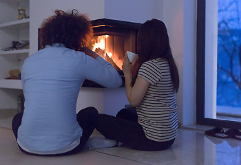 Image showing happy multiethnic couple sitting in front of fireplace