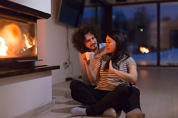 Image showing happy multiethnic couple sitting in front of fireplace