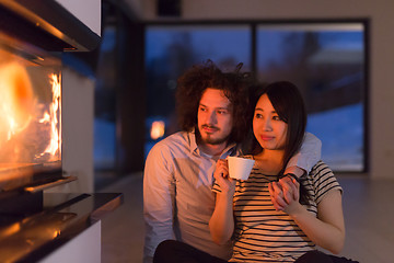 Image showing happy multiethnic couple sitting in front of fireplace