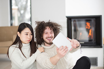 Image showing multiethnic couple using tablet computer in front of fireplace