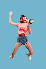 Image showing Beautiful young woman jumping with megaphone isolated over blue background