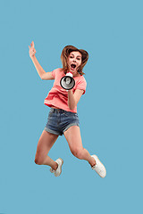 Image showing Beautiful young woman jumping with megaphone isolated over blue background