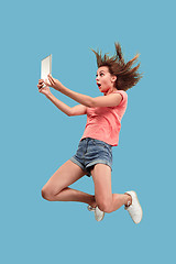 Image showing Image of young woman over blue background using laptop computer or tablet gadget while jumping.