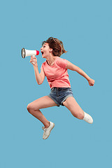 Image showing Beautiful young woman jumping with megaphone isolated over blue background