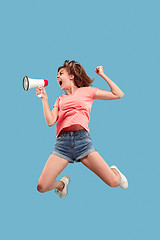 Image showing Beautiful young woman jumping with megaphone isolated over blue background