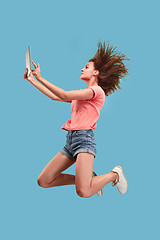 Image showing Image of young woman over blue background using laptop computer or tablet gadget while jumping.