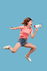 Image showing Beautiful young woman jumping with megaphone isolated over blue background