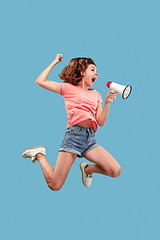 Image showing Beautiful young woman jumping with megaphone isolated over blue background