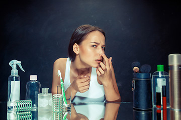 Image showing Unsatisfied young woman looking at her self in mirror on black background