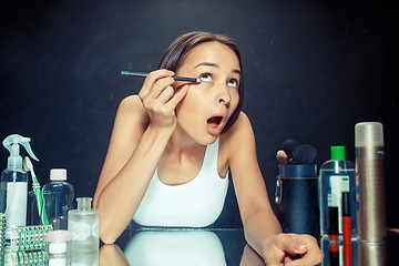 Image showing Beauty woman applying makeup. Beautiful girl looking in the mirror and applying cosmetic with a Eyeliner.