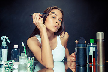 Image showing Beauty woman applying makeup. Beautiful girl looking in the mirror and applying cosmetic with a brush.