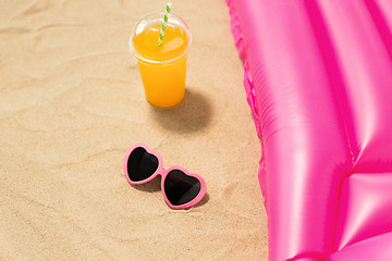 Image showing sunglasses, juice and pool mattress on beach sand