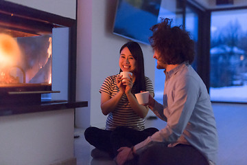 Image showing happy multiethnic couple sitting in front of fireplace