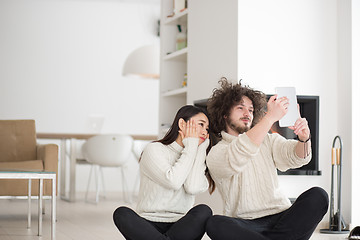 Image showing multiethnic couple using tablet computer in front of fireplace