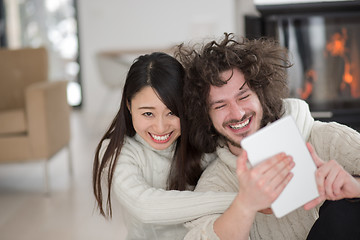 Image showing multiethnic couple using tablet computer in front of fireplace