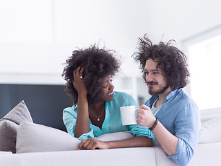 Image showing multiethnic couple sitting on sofa at home drinking coffe