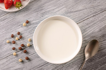 Image showing Cereal balls, a plate plate of milk and a strawberry on a gray wooden table. Top view