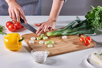 Image showing Woman\'s hands cut green leek on a wooden board on the kitchen table with various fresh vegetables. Step by Step Salad Cooking