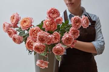 Image showing A girl in a brown apron holds a vase with pink roses on a gray background. Flower concept. Gift for celebration