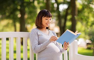 Image showing happy pregnant asian woman reading book at park