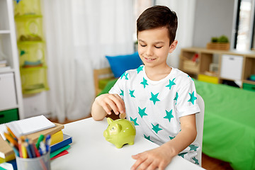 Image showing little boy putting coin into piggy bank at home