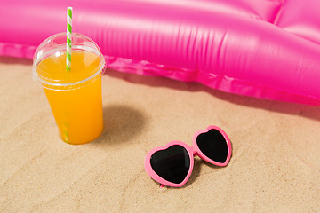 Image showing sunglasses, juice and pool mattress on beach sand