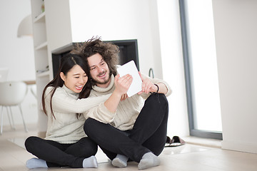 Image showing multiethnic couple using tablet computer in front of fireplace