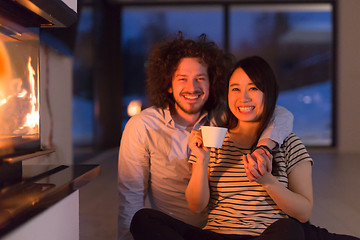 Image showing happy multiethnic couple sitting in front of fireplace