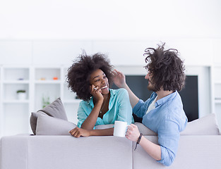 Image showing multiethnic couple sitting on sofa at home drinking coffe