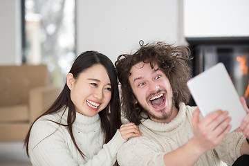 Image showing multiethnic couple using tablet computer in front of fireplace