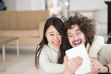 Image showing multiethnic couple using tablet computer in front of fireplace