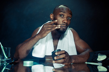 Image showing young man in bedroom sitting in front of the mirror after scratching his beard