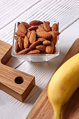 Image showing Natural ingredients for healthy breakfast- almonds in a glass bowl and fresh banana on a wooden board on a gray background. Vegetable protein for vegans.