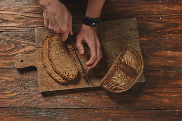 Image showing Hands of young man cut dark bread