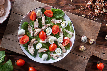 Image showing Healthy freshly prepared salad of quail eggs, meat, tomatoes and spinach in a plate on a wooden board on the kitchen table. Dietary lunch. Flat lay