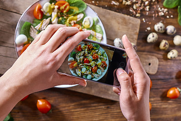 Image showing Hands of a girl with a phone make a photo of a freshly prepared salad. Food blogging concept. Top view