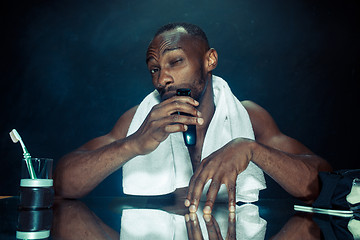 Image showing young man in bedroom sitting in front of the mirror scratching his beard