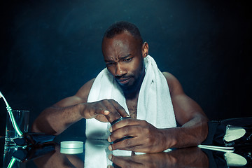 Image showing young man in bedroom sitting in front of the mirror after scratching his beard