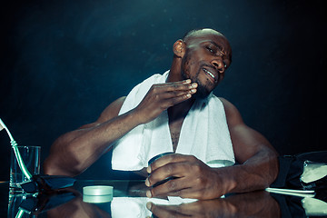 Image showing young man in bedroom sitting in front of the mirror after scratching his beard