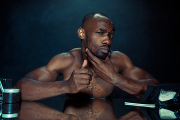 Image showing young man in bedroom sitting in front of the mirror after scratching his beard