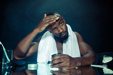 Image showing young man in bedroom sitting in front of the mirror after scratching his beard